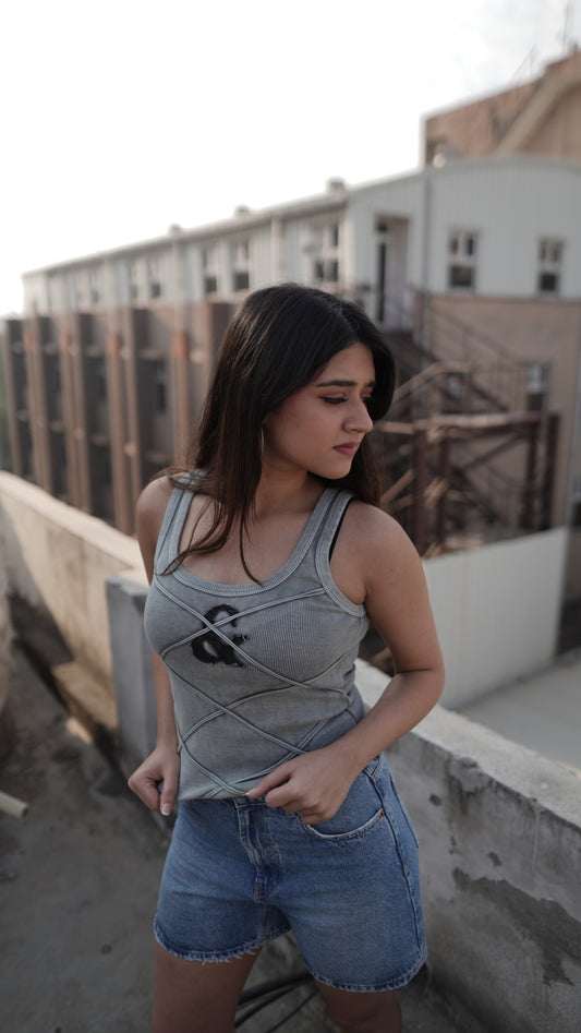 A woman wearing a gray tank top with a denim logo and body contouring exposed seam detailing, paired with blue denim shorts.