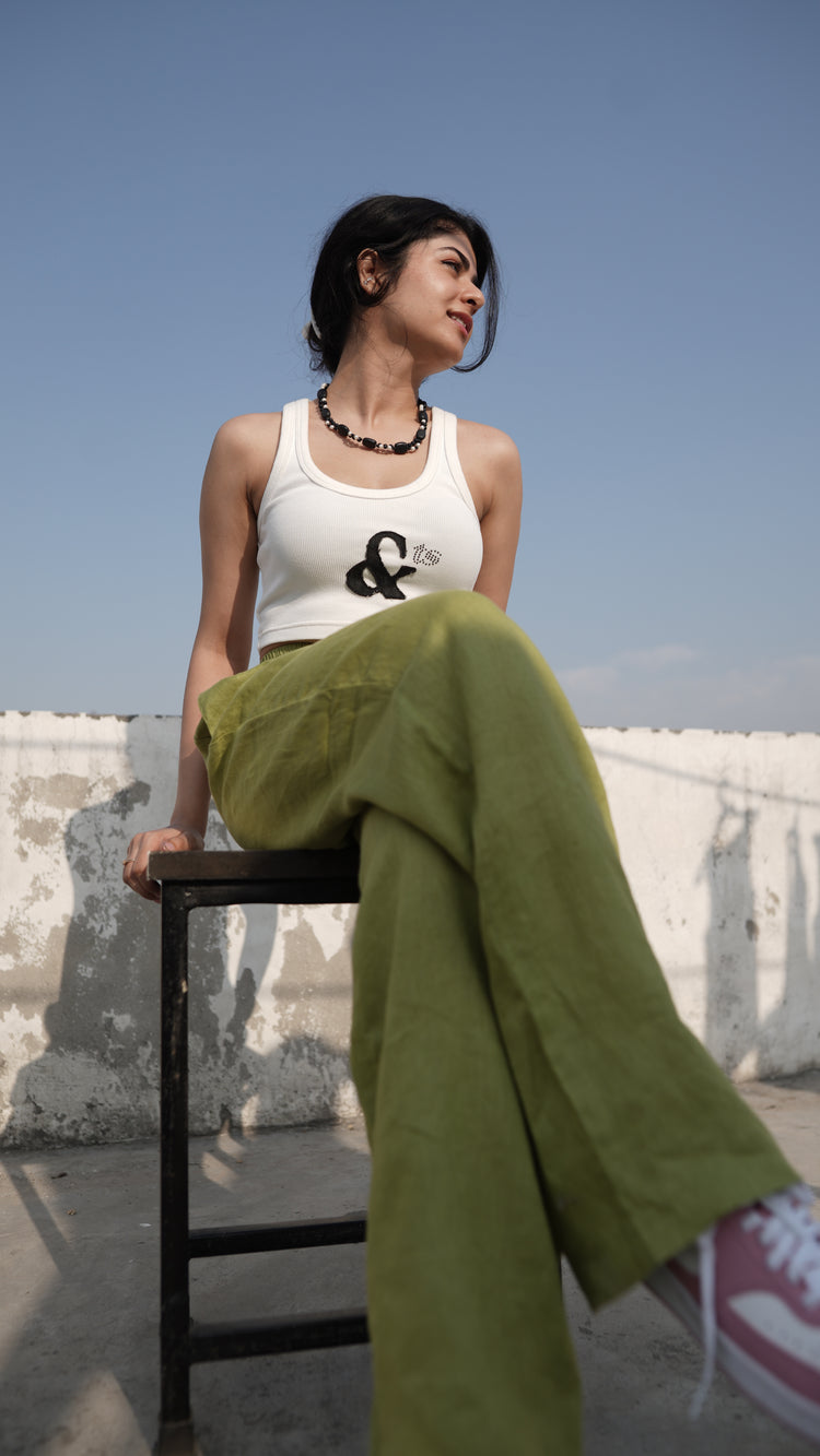 A person wearing an off-white tank top with a denim patch logo and rhinestone embellishments, paired with green pants.