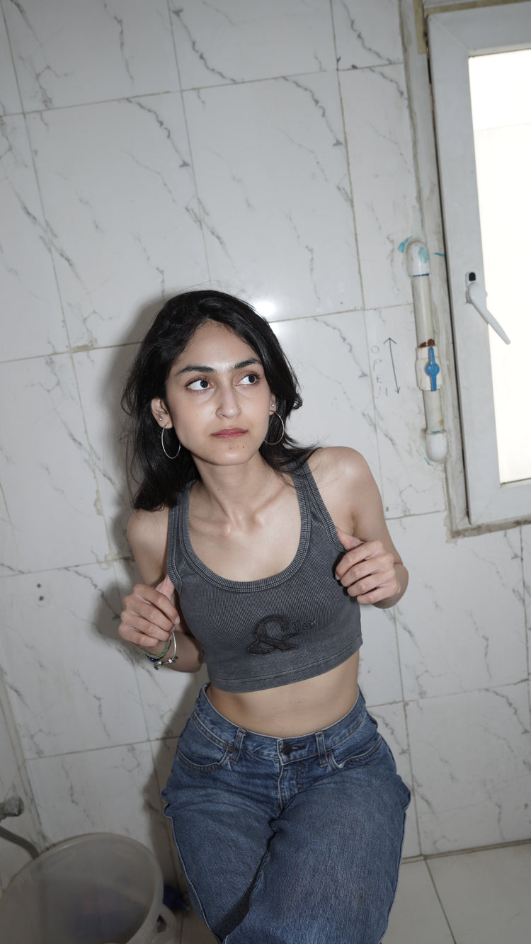 A person wearing a dark gray tank top with a denim patch logo and rhinestone embellishments.