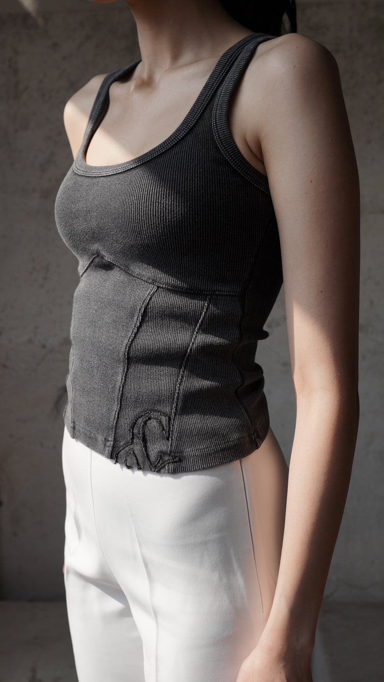 A person wearing a black tank top and white trousers. The tank top is the main focus, showing a contoured design with a cinched waist.