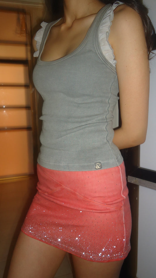 A person wearing a shell pink mini skirt with rhinestones, paired with a gray tank top.