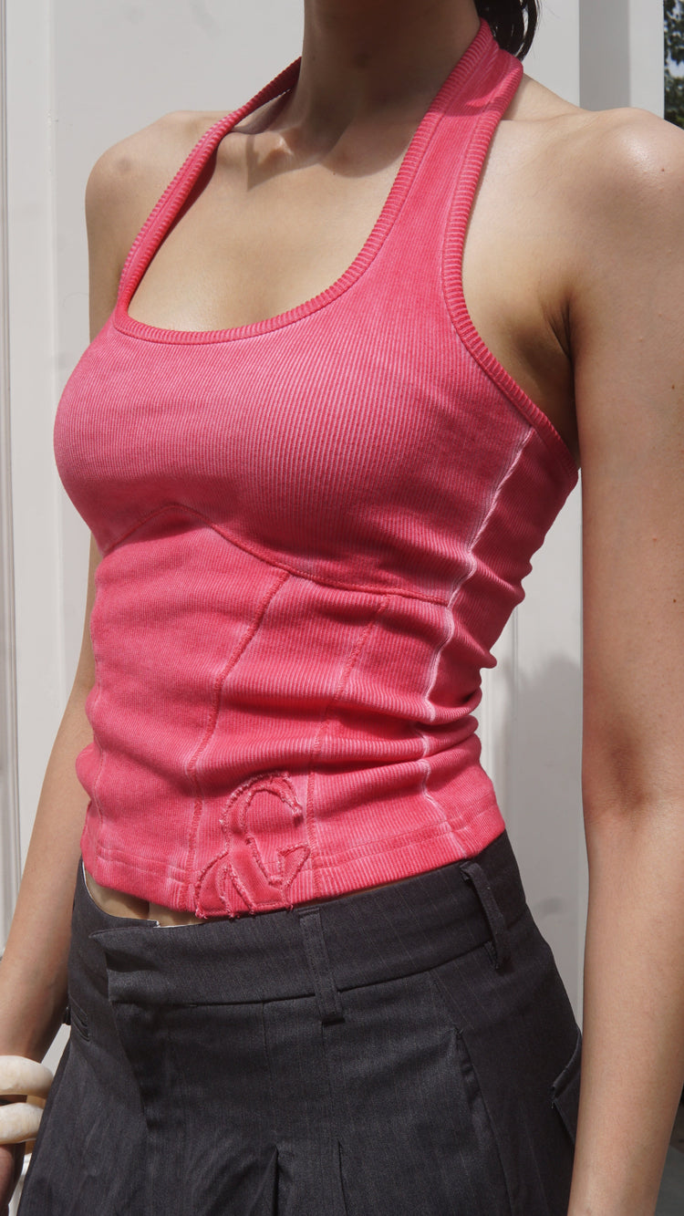 Person wearing a pink halter neck tank top and black pants on a white background