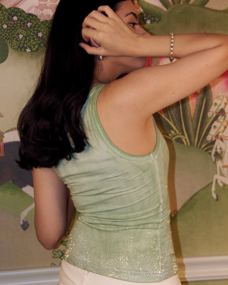 Woman wearing a green sequined top in front of a decorative wall.