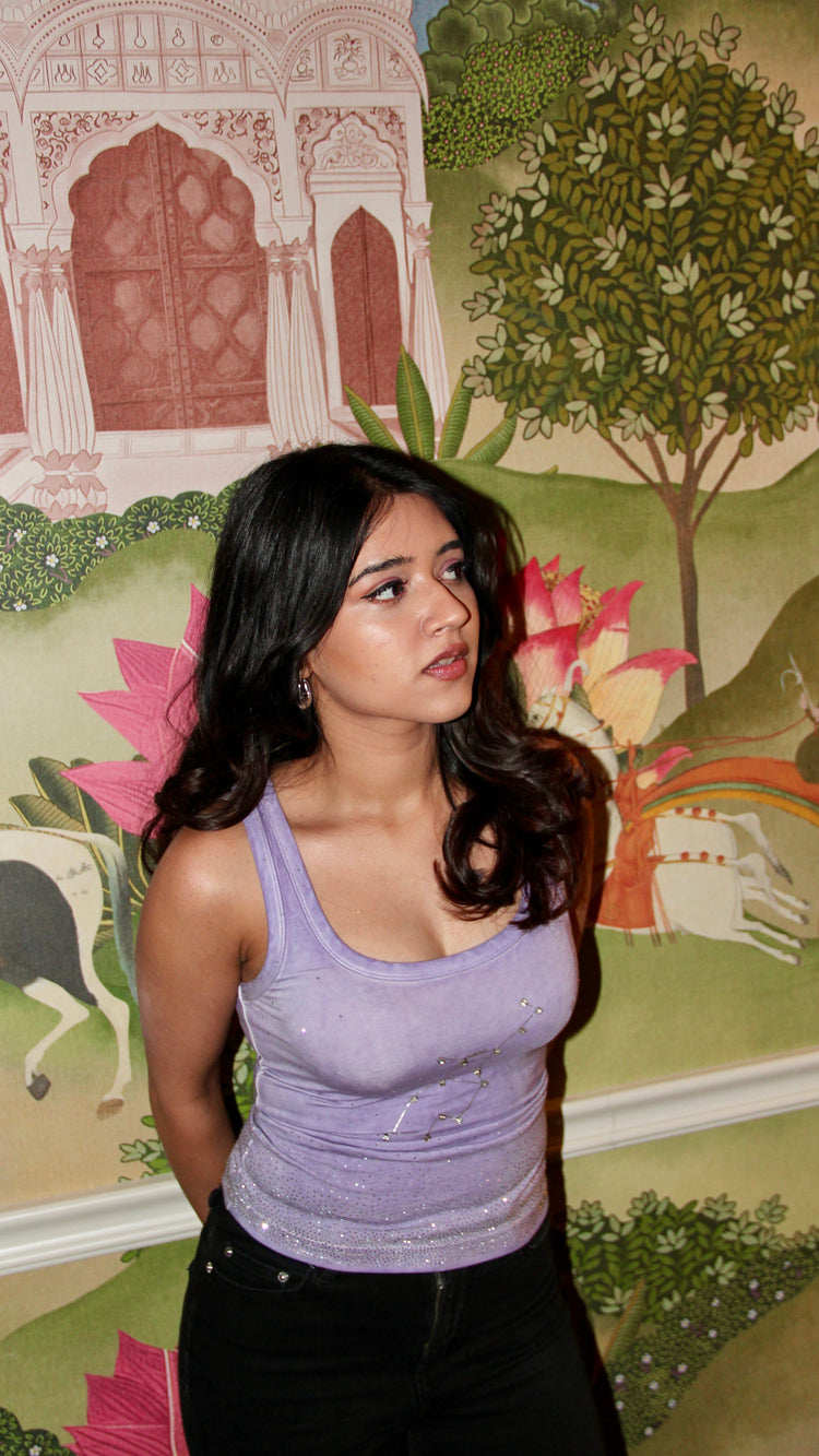 Woman in a purple top standing in front of a decorative wall with artistic designs.