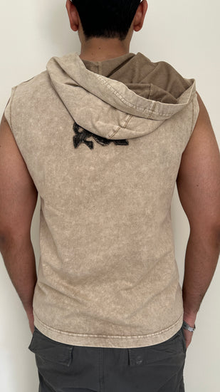 Person wearing a beige sleeveless hoodie with a hood against a plain background