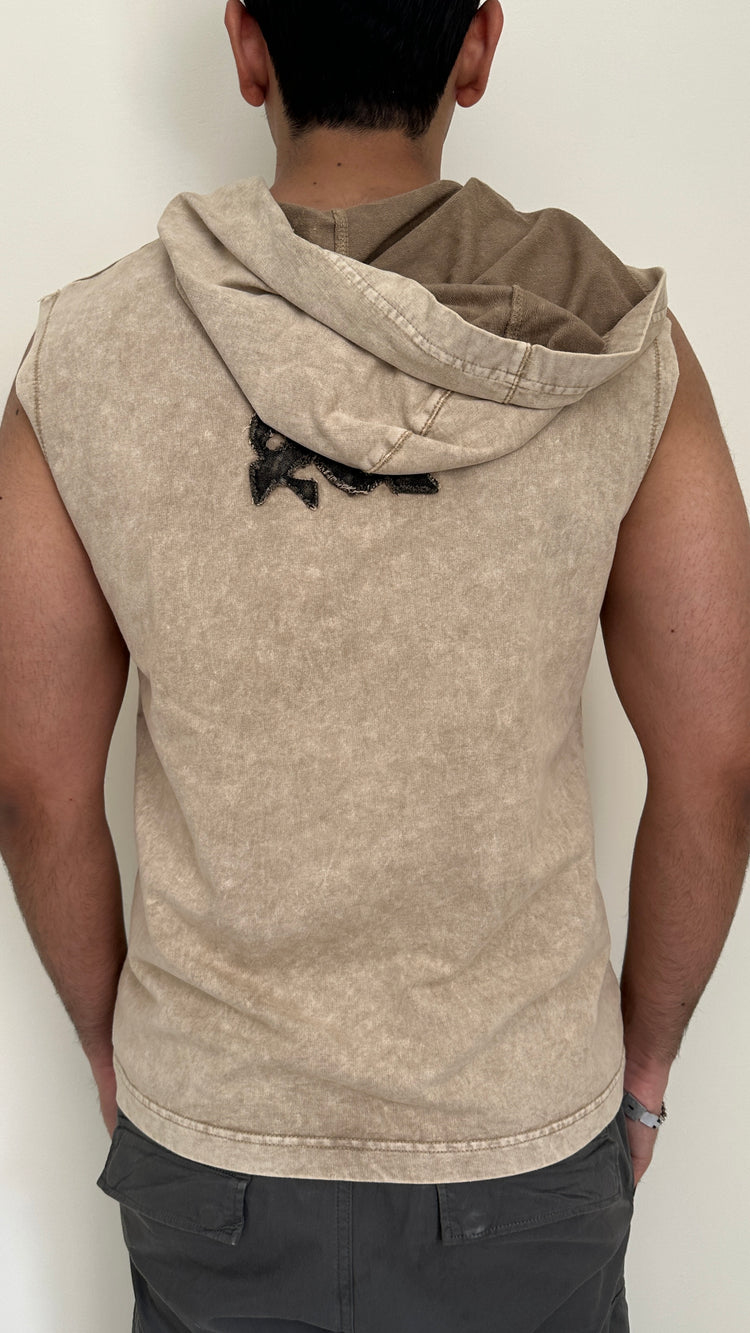 Person wearing a beige sleeveless hoodie with a hood against a plain background