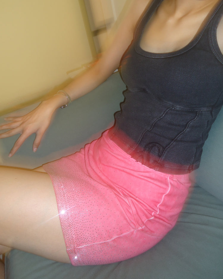 Woman wearing a pink skirt and a black tank top sitting on a couch