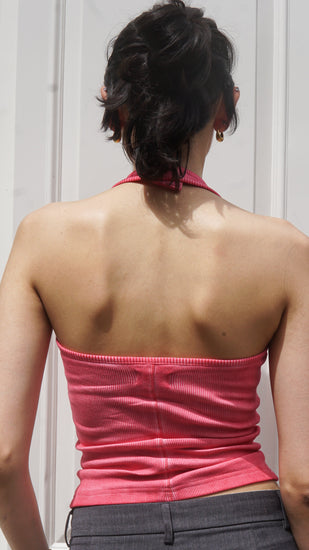 Person wearing a pink halter neck tank top and gray pants against a white wall