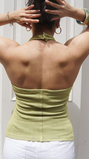 Person wearing a green halter neck tank top with their back to the camera, standing against a white background.