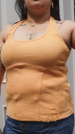 Person wearing an orange halter neck tank top and blue jeans.