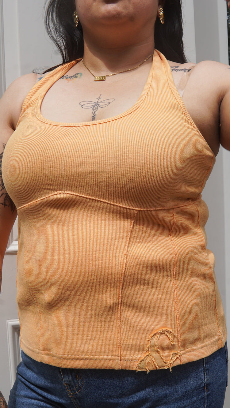 Person wearing an orange halter neck tank top and blue jeans.
