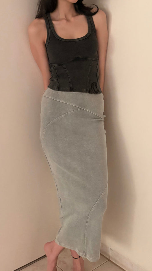 Person wearing a black top and light gray skirt against a plain wall.