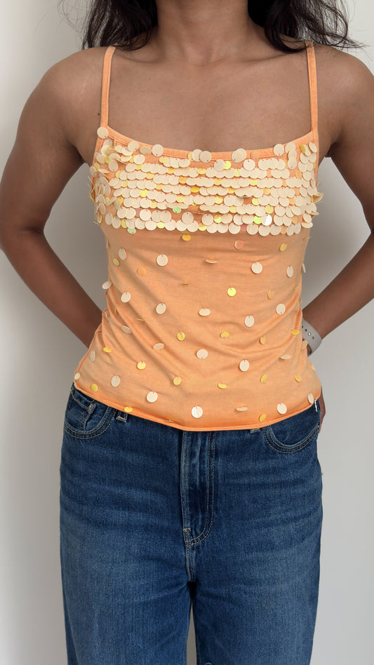Person wearing an orange sequined camisole top and blue jeans on a plain background