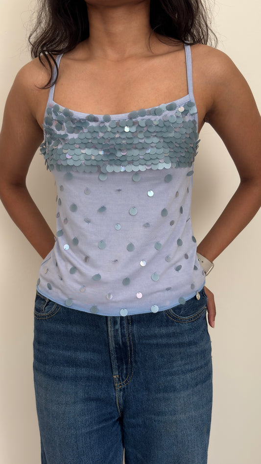 Model wearing a sequined blue camisole top and jeans against a plain background