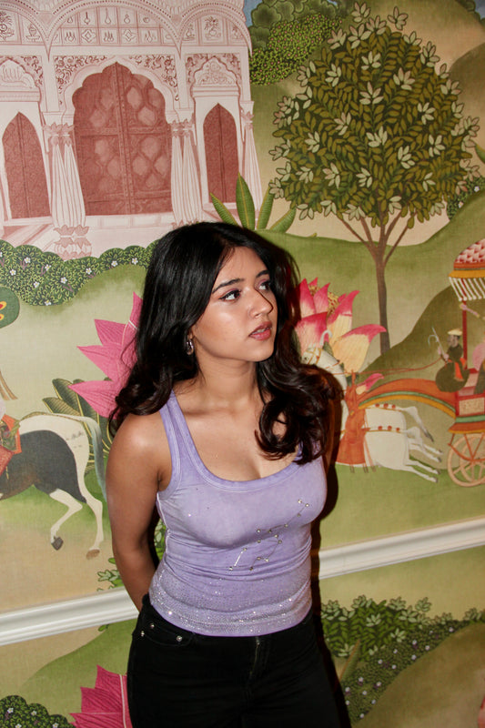 Woman in a purple top standing in front of a decorative wall with artistic designs.